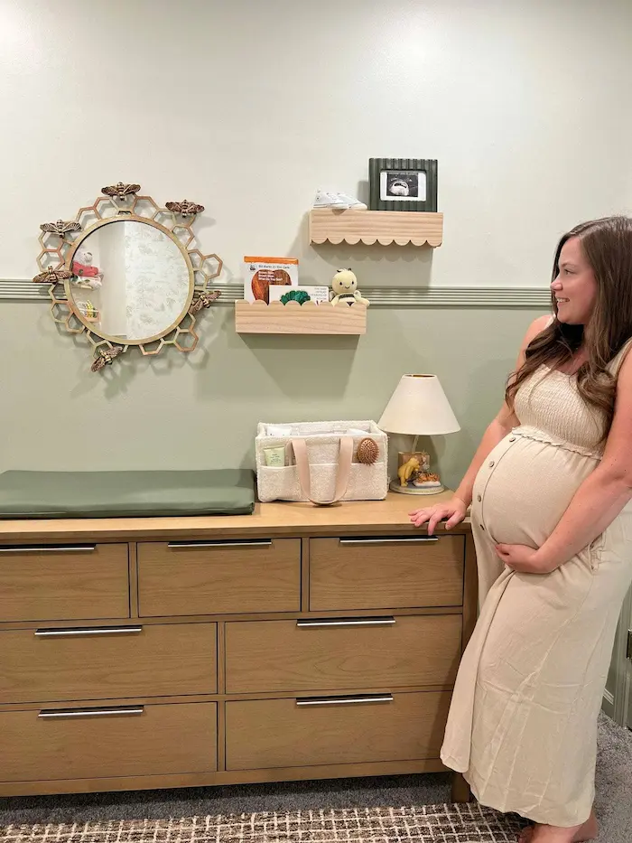 A low dresser converted into a changing station with a caddy organizer on the wall above holding diapers, wipes, and creams within easy reach