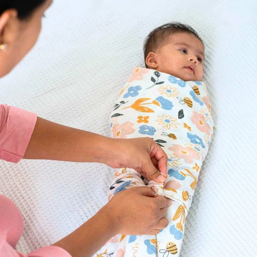 A mother’s hands gently swaddling a newborn in a muslin blanket on a safe, flat sleep surface