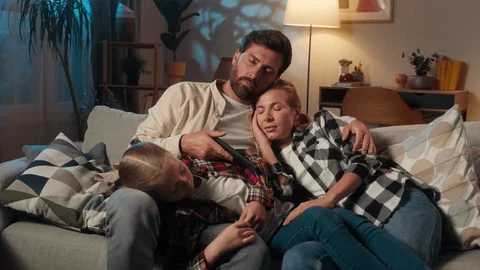 A parent holding a sleeping newborn while sitting next to their partner on the couch