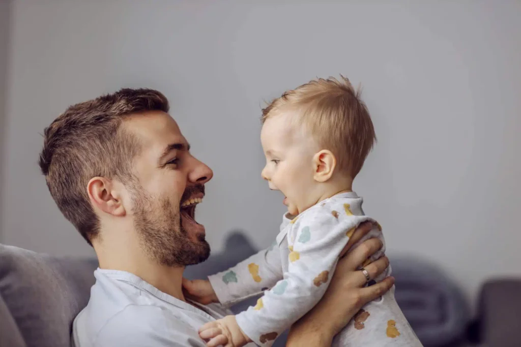 A parent leaning close to a newborn’s face, smiling and talking. Caption: Early face-to-face interaction using “parentese” captures a baby’s attention and lays the groundwork for conversation.