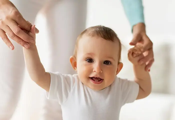  A parent’s hands supporting a newborn upright, feet touching a mat, demonstrating the stepping reflex.