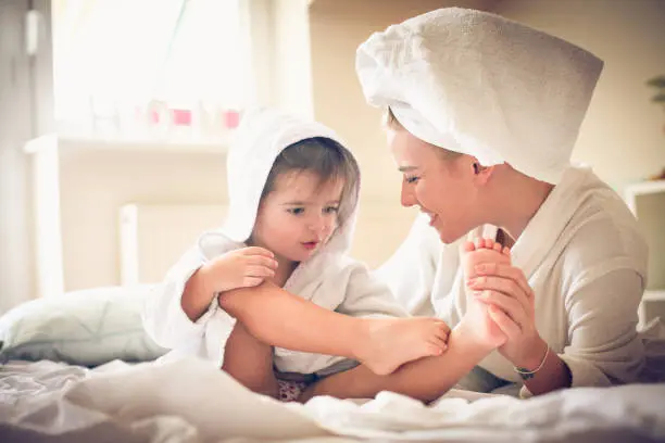 A serene photo of a parent massaging lotion onto a happy baby’s feet after a bath, with a damp towel in the background