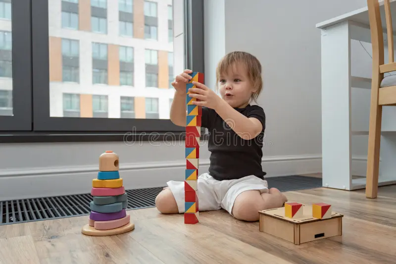 A toddler playing with a wooden block tower and a simple shape puzzle on the floor.