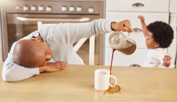 Image of a parent looking exhausted while holding a coffee cup near a sleeping baby
