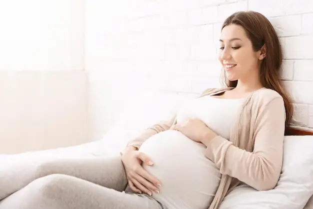 Image of a pregnant woman resting her hands on her belly, appearing focused and aware